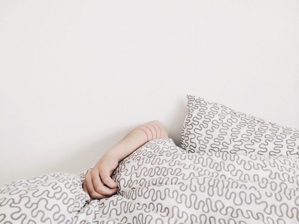 A woman's hand on top of the sheets while tucked into bed 