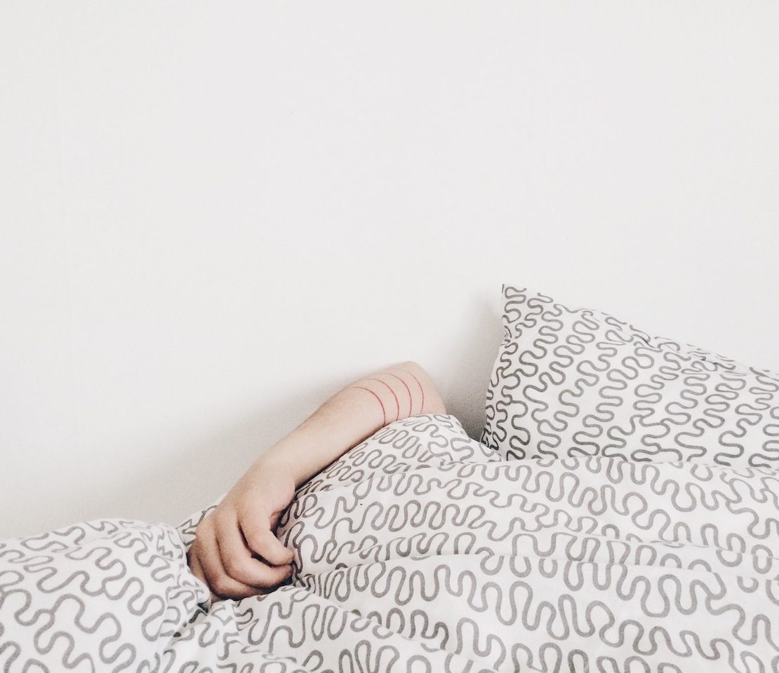 A woman's hand on top of the sheets while tucked into bed