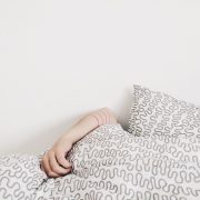A woman's hand on top of the sheets while tucked into bed