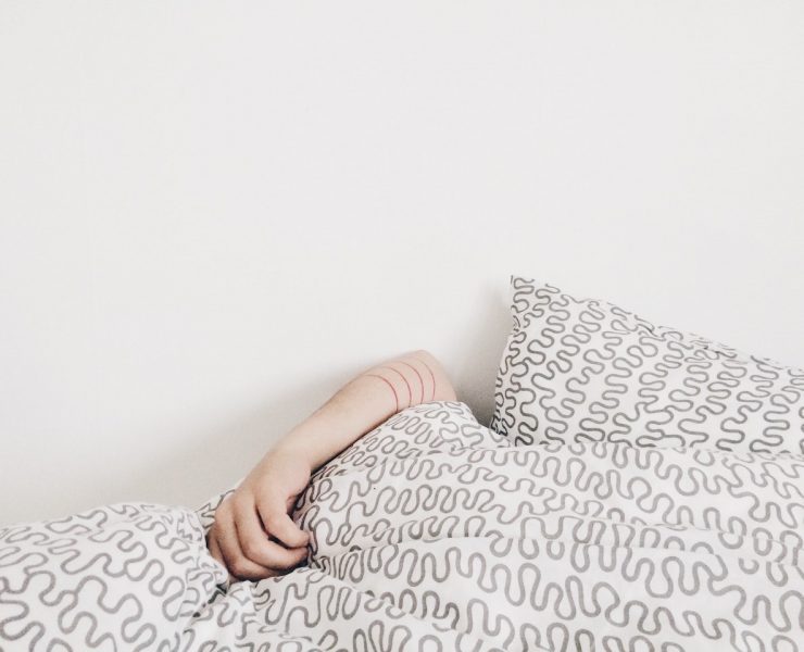 A woman's hand on top of the sheets while tucked into bed