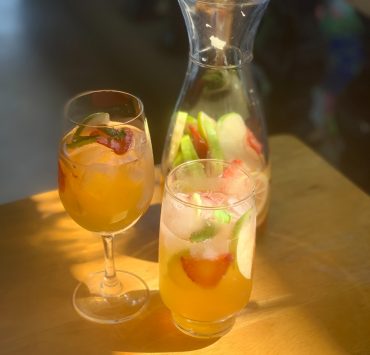 A photo of white wine sangria with apples, strawberry and lemons in a carafe and two glasses. Photo by Pauline Miranda for Nolisoli