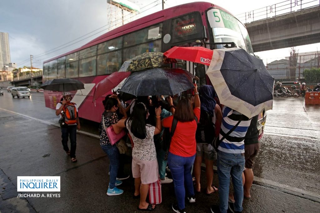commuters trying to board a bus in the rain in EDSA