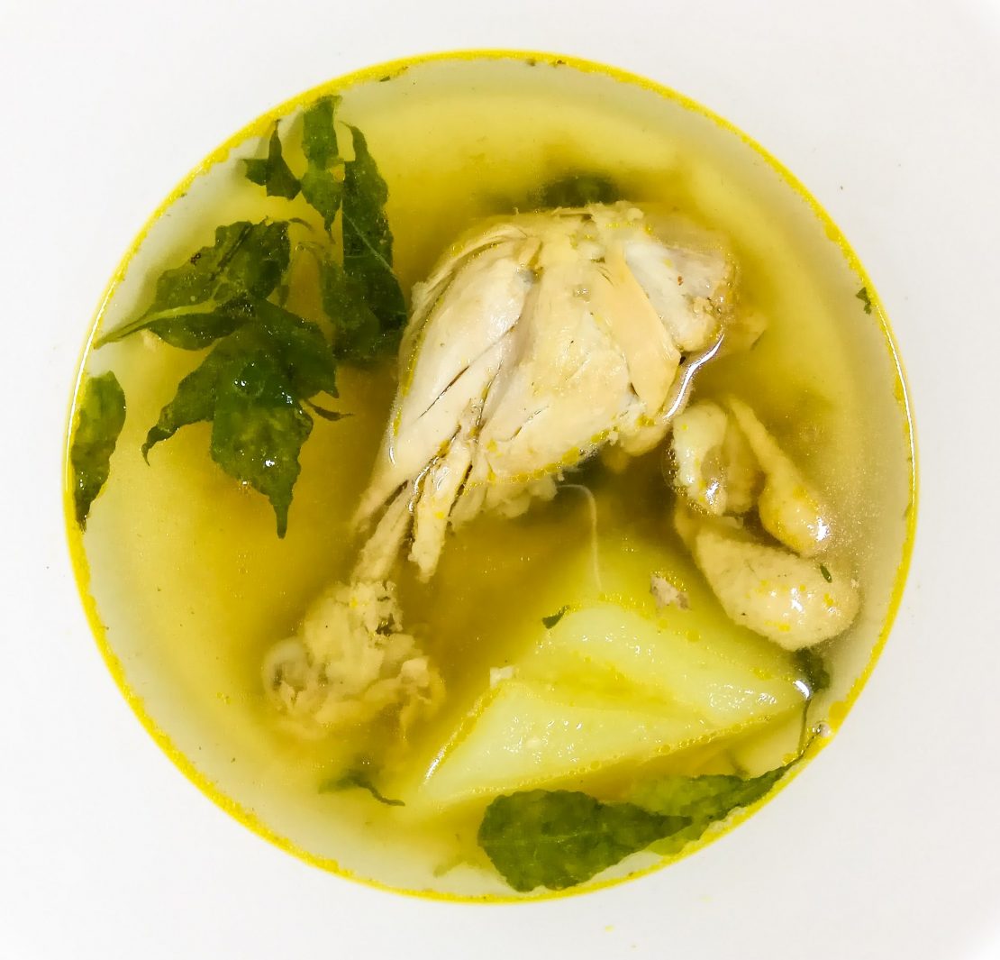 chicken drumstick in a bowl with broth, papaya slice, chili leaves