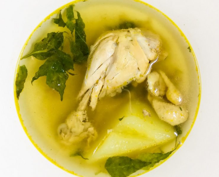 chicken drumstick in a bowl with broth, papaya slice, chili leaves