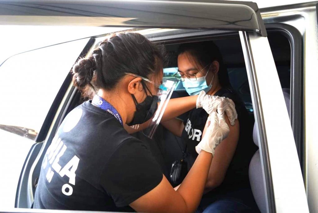 a health worker administering covid-19 vaccine on a passenger inside a car
