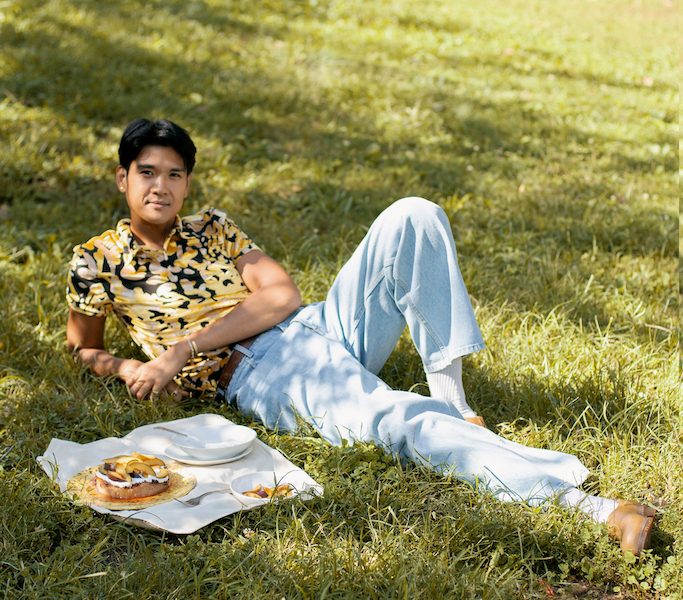 woldy reyes laying in the grass at fort green park in brooklyn with a baked good on a picnic cloth