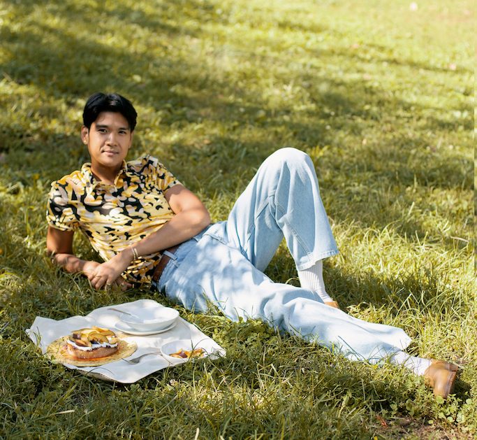 woldy reyes laying in the grass at fort green park in brooklyn with a baked good on a picnic cloth