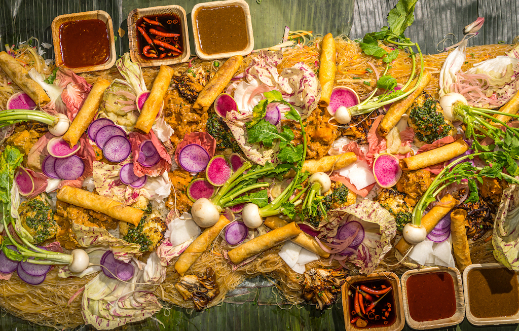 a mound of filipino food laid in banana leaf for a kamayan feast with pancit, rice, and lumpia and fresh produce